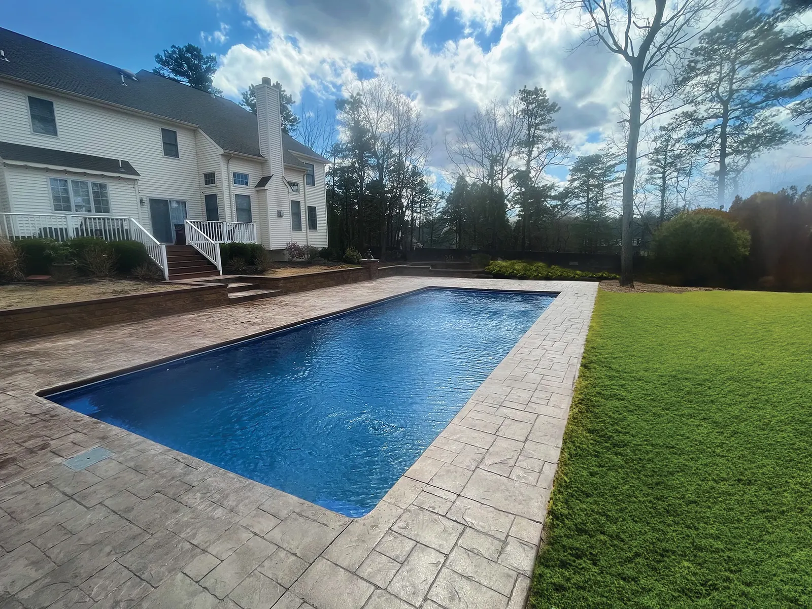 Inground fiberglass pool with a paver deck behind an upscale Ohio home